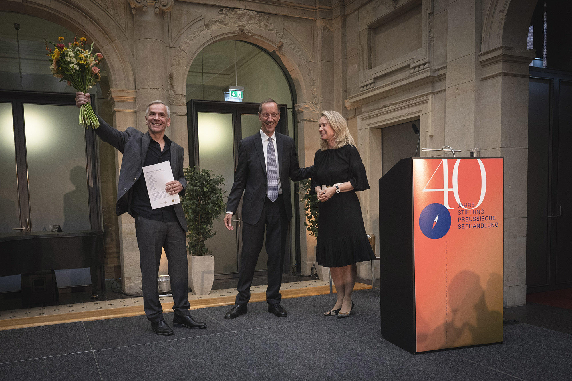 Lutz Seiler nimmt Blumen und Urkunde entgegen, rechts: Dr. Hans Gerhard Hannesen und Sarah Wedl-Wilson