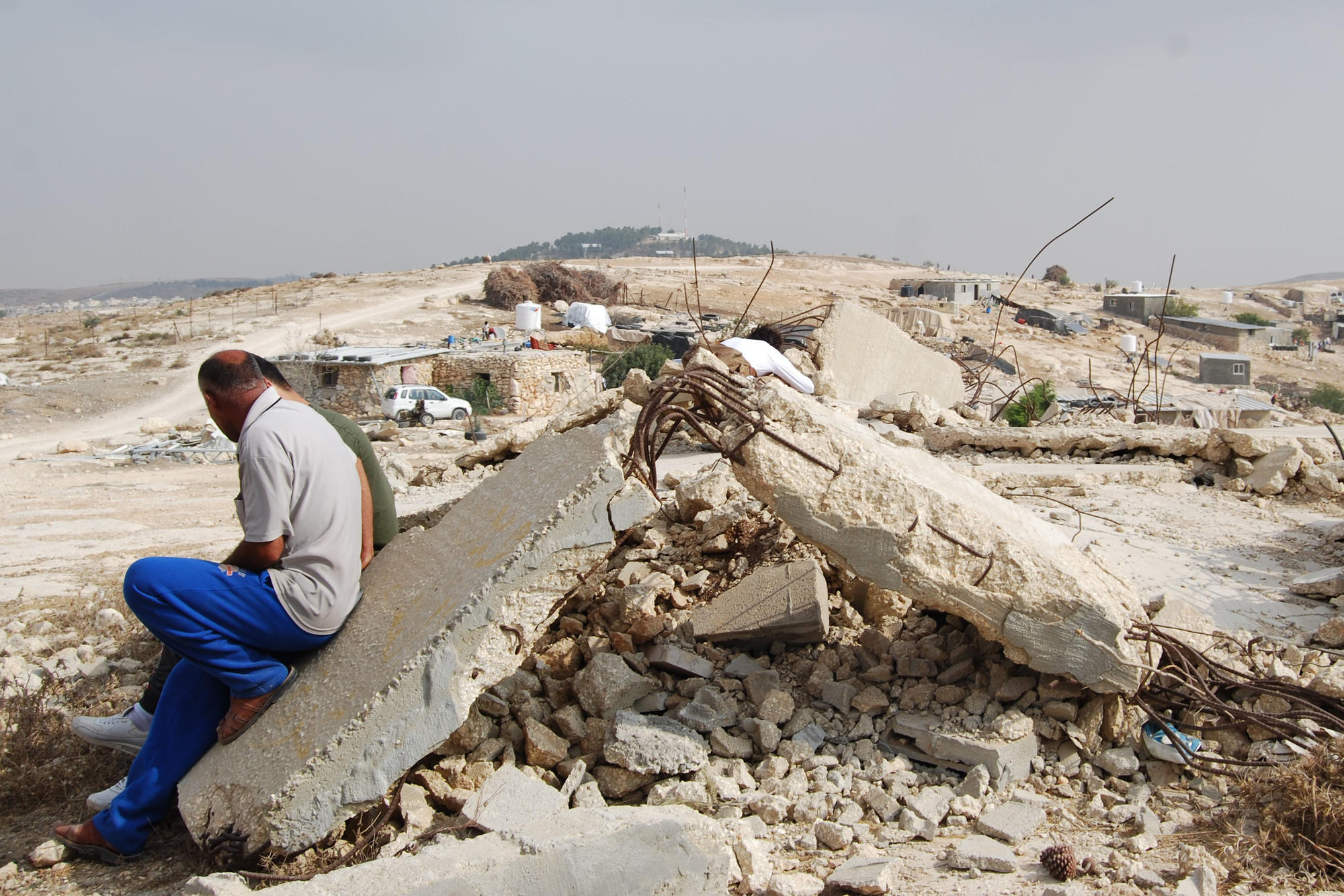Zwei Männer sitzen auf den Ruinen der Moschee ihres Dorfes. Israel Defense Forces haben sie zerstört, weil Palästinenser sie ohne Baugenehmigung gebaut haben. Eine Genehmigung bekommen sie nicht, weil das Gebiet zur Militärzone erklärt wurde.
