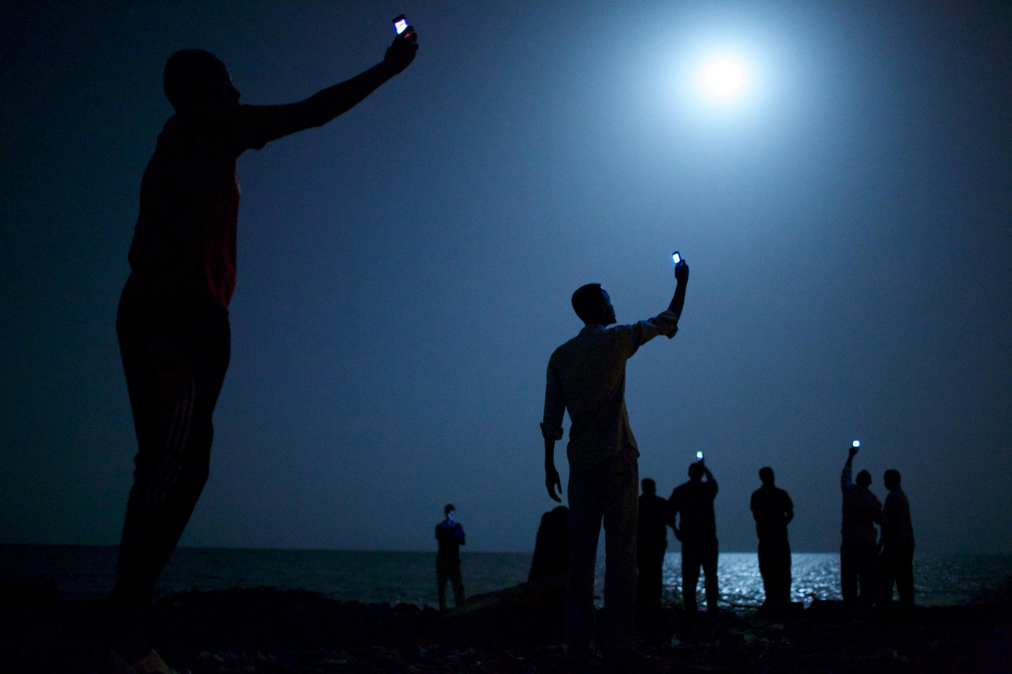 Afrikanische Flüchtlinge versuchen am Strand von Dschibuti ein Handysignal aus ihrer Heimat zu bekommen. 2014 erhält John Stanmeyer für diese Aufnahme den World Press Photo Award.