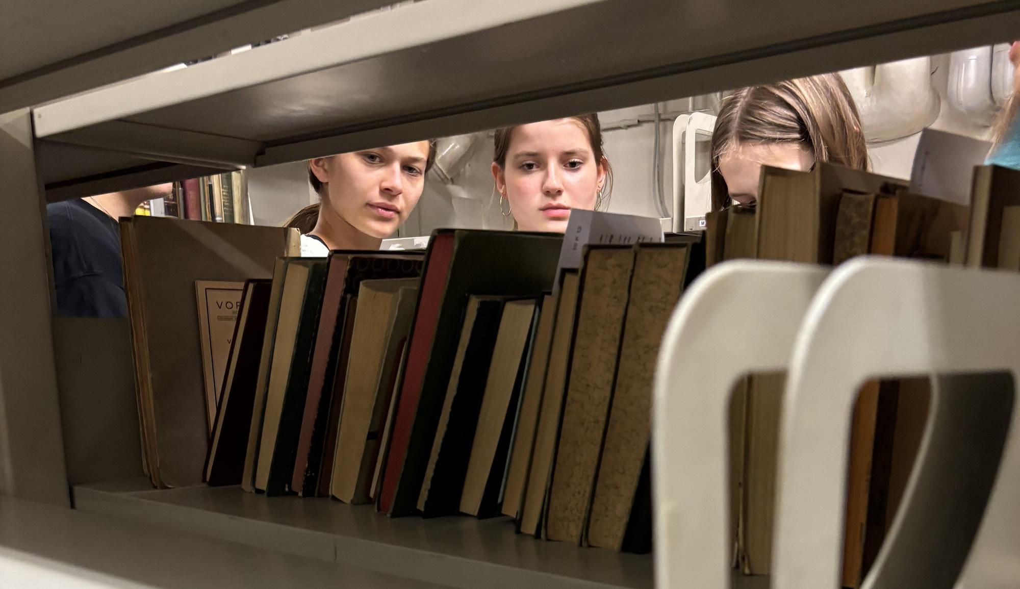 Die Schülerinnen wählen am Regal Bücher für die Recherche aus.